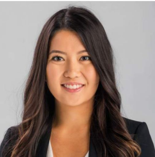 Headshot of a smiling person with long dark hair wearing a black blazer on a gray background