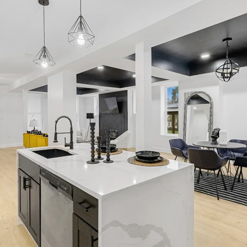 Bright modern kitchen and dining area with white island, black accents, and pendant lights