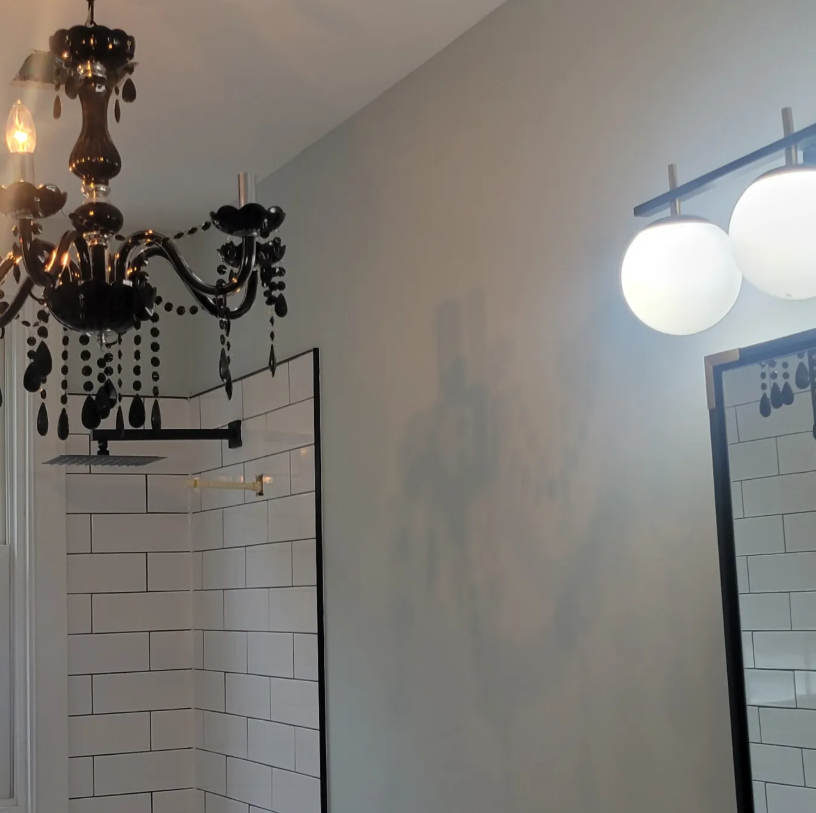 Bathroom with white subway tiles, black chandelier, and round vanity lights beside a mirror.