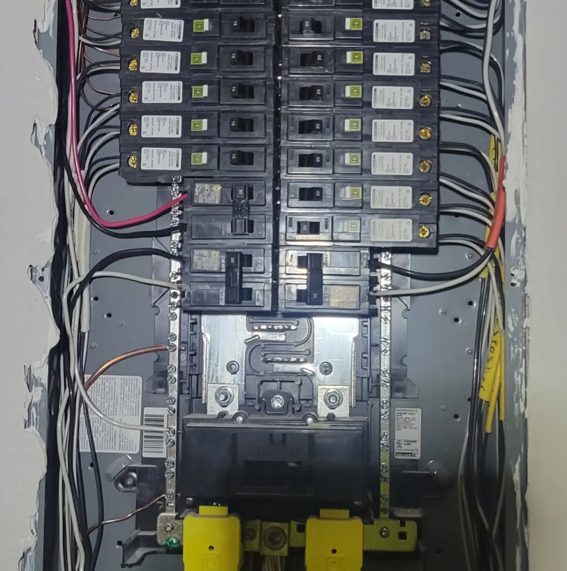 Open electrical breaker panel with rows of black switches and multicolored wiring inside a gray cabinet