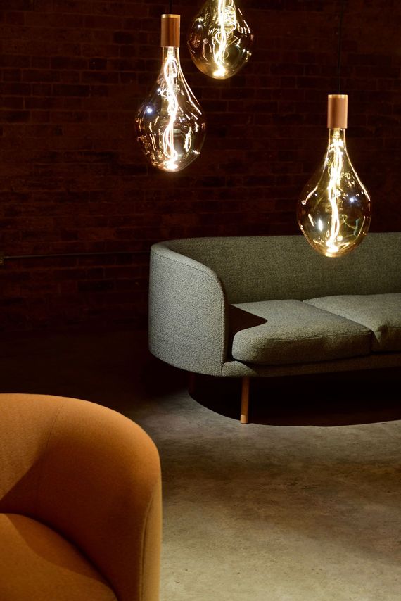 Dim lounge with a gray sofa, warm hanging pendant lights, and a blurred orange chair in the foreground