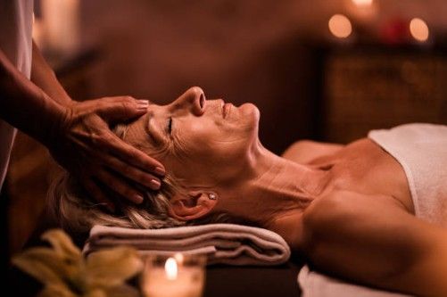Woman receiving a facial massage with a towel under her head in a warm spa setting