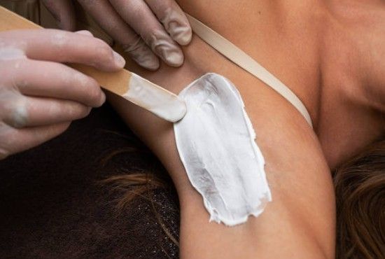 Applying white cream to a person’s upper arm with a wooden spatula