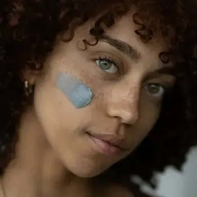 Close-up portrait of a person with curly hair and blue face paint on one cheek