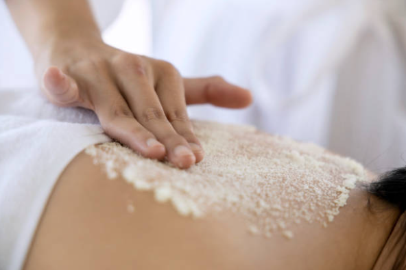 Hand massaging a white granular body scrub onto a person's bare back