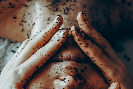 Hands rubbing a person’s face with speckled black exfoliating scrub product