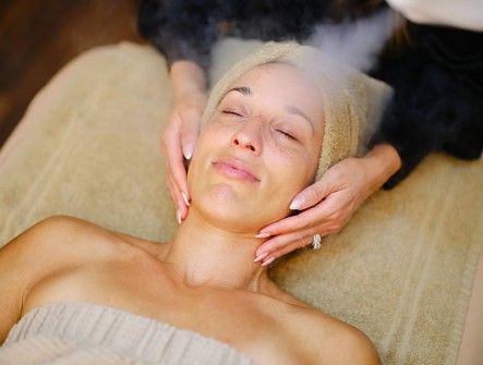 Woman receiving a facial massage on a spa treatment bed, eyes closed, with a towel wrapped around her head