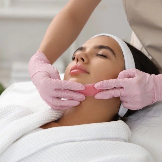 Woman receiving a facial massage with pink-gloved hands in a spa setting