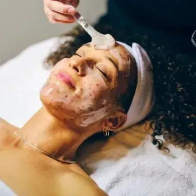 Woman receiving facial treatment with a brush while lying on a spa bed