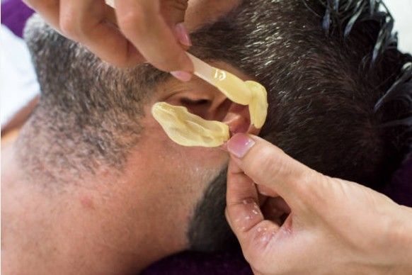 Hands fit clear hearing aid onto a person’s ear close-up