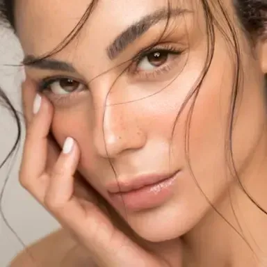 Close-up portrait of a person with soft makeup, hand on face, and loose strands of hair