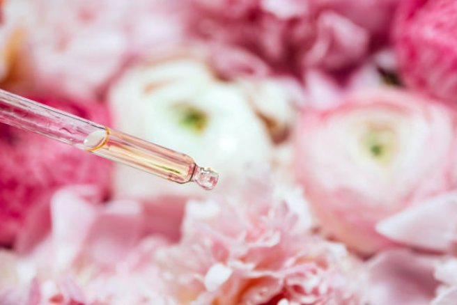 Pink pipette with golden liquid above soft pink and white flowers