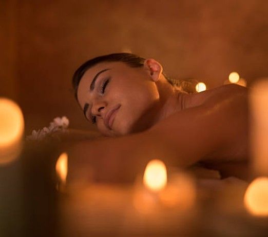 Person resting in a candlelit spa, eyes closed, with soft warm lights and blurred candles in the foreground