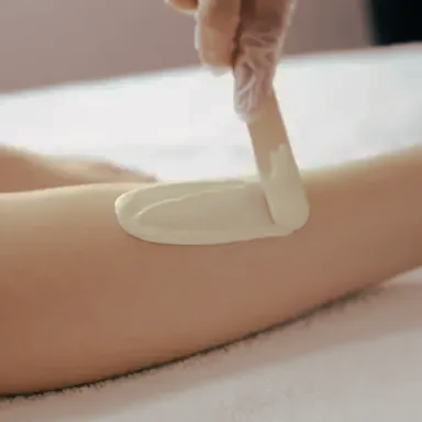 Spatula spreading creamy lotion on a person's arm in a spa setting