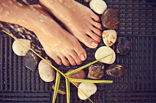 Bare feet resting on pebbles with bamboo leaves on a woven mat, spa-like setting