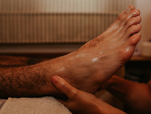 Person receiving a foot massage on a towel, with hands supporting the raised foot.