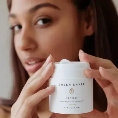 Woman holding a white skincare jar labeled “Sreen Envee Protect” near her face
