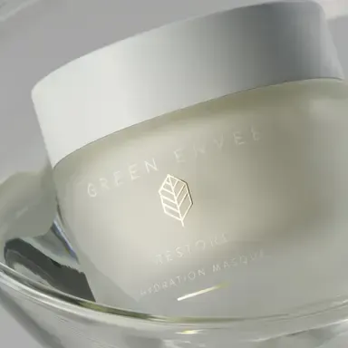 Frosted green skincare jar with white lid resting on a glass dish