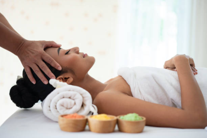 Spa therapist giving a head massage to a woman lying on a table with rolled towels and bowls nearby