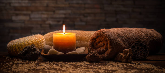 Two lit candles between rolled brown blankets on a textured surface, warm dim light