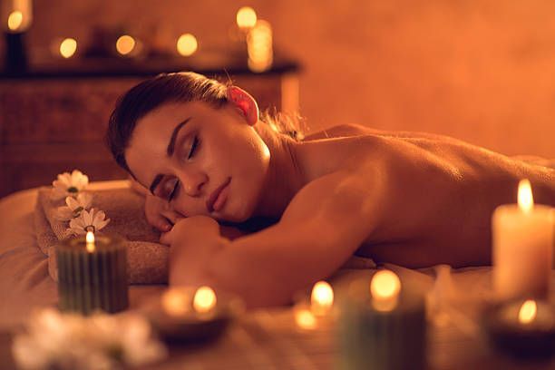Person relaxing in a candlelit spa with eyes closed, surrounded by warm orange lighting