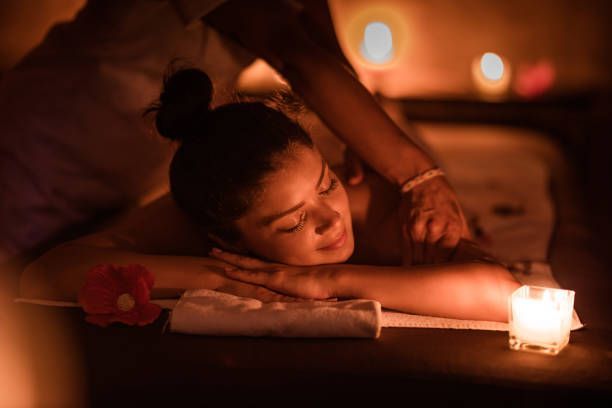 Person receiving a candlelit back massage in a dim, warm spa setting