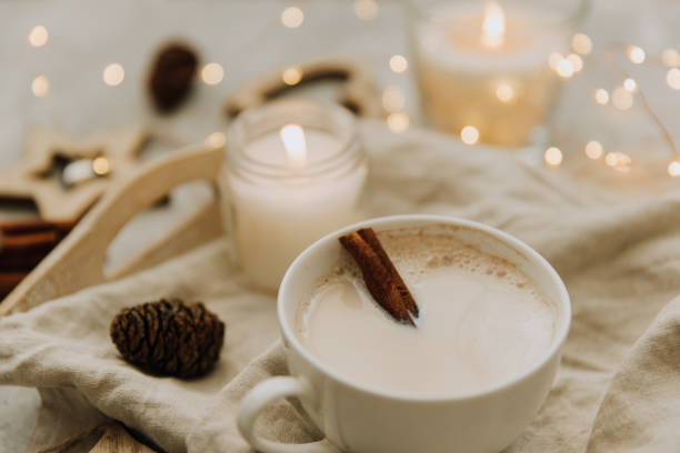 Cozy candlelit scene with a cup of coffee, cinnamon stick, pinecone, and soft beige fabric