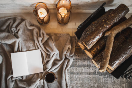 Cozy tabletop scene with candles, books, a blank card, coffee, and a soft gray throw on wood surface