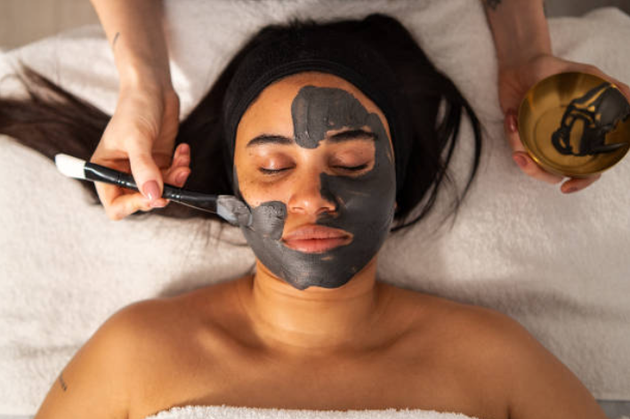 Person lying down with a black facial mask being applied by a brush during a spa treatment