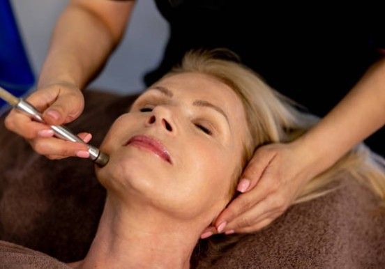 Facial spa treatment with a technician applying a massage tool to a relaxed client