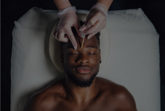 Person receiving a facial massage with hands on forehead while lying on a treatment bed, eyes closed.