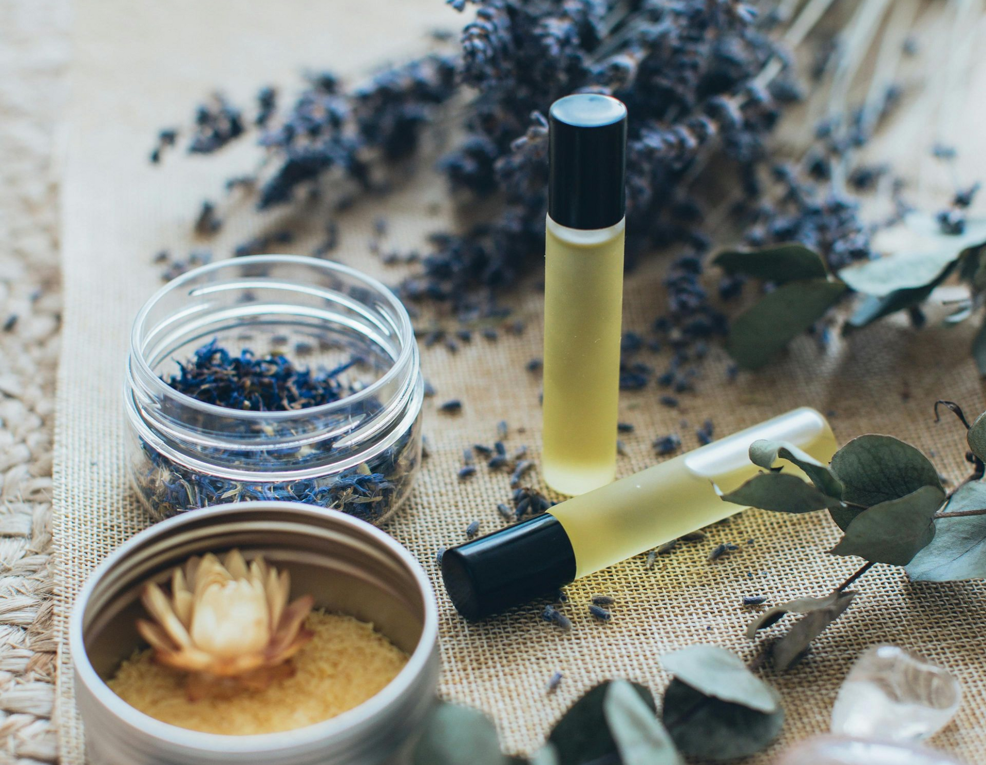 Aromatic skincare items with serums, cream, and dried flowers on a textured cloth