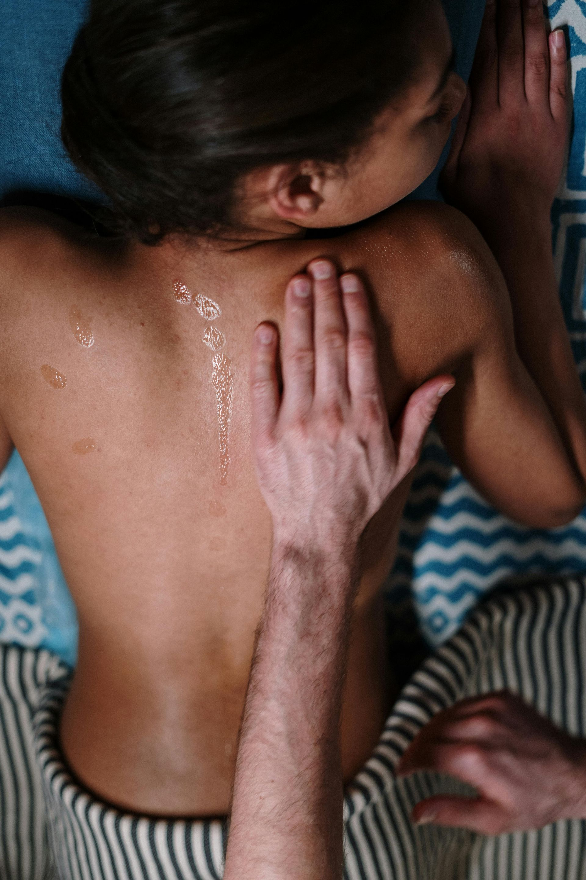 Hand pressing on a person's bare back with water droplets, suggesting a massage or back rub