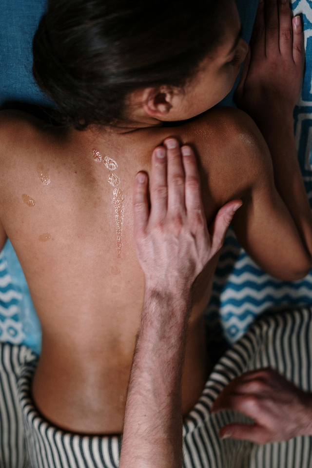Hand pressing on a person's bare back with water droplets, suggesting a massage or back rub