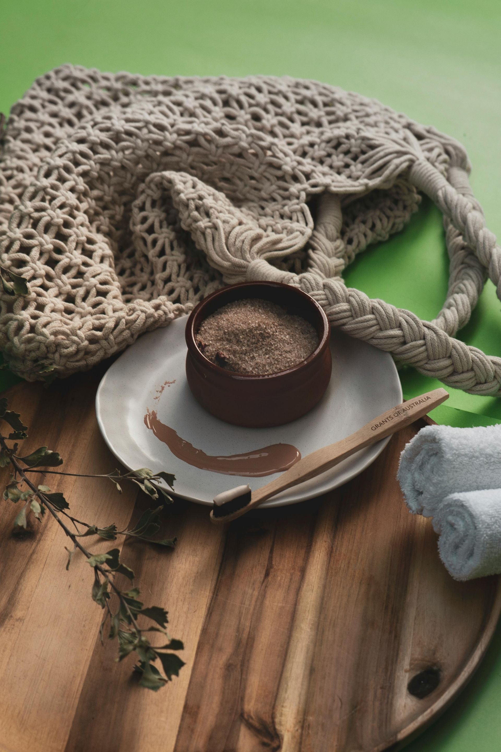 Rustic breakfast scene with coffee in a brown cup, wooden board, cloth napkin, and knitted blanket on a green background