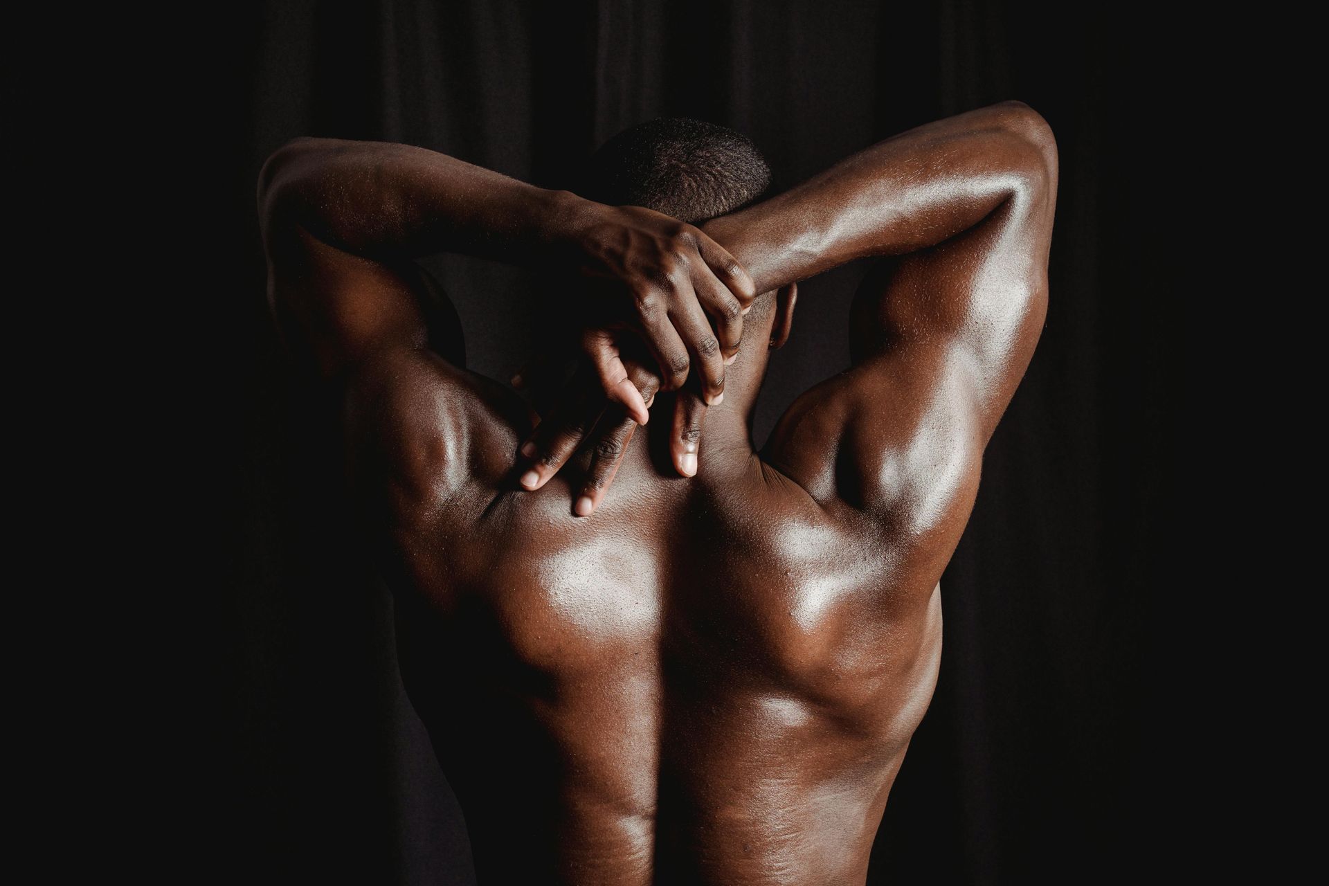 Person from behind, arms raised behind head, showing muscular back against a dark background