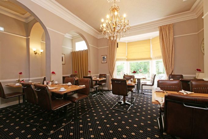 A hotel breakfast room with tables, chairs, floral arrangements, and a chandelier.