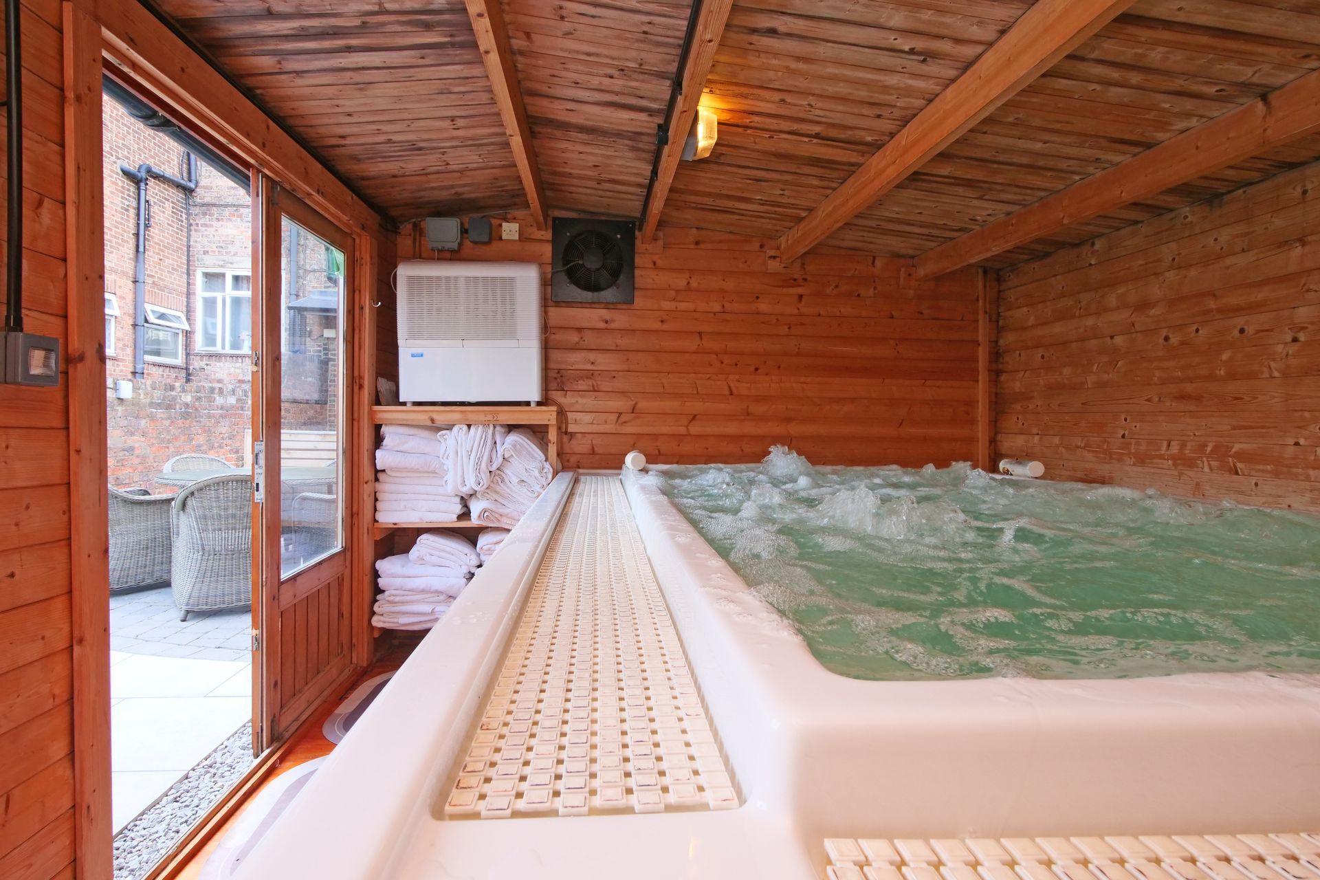Wooden cabin with jacuzzi, white towels, and exterior view through open glass door.