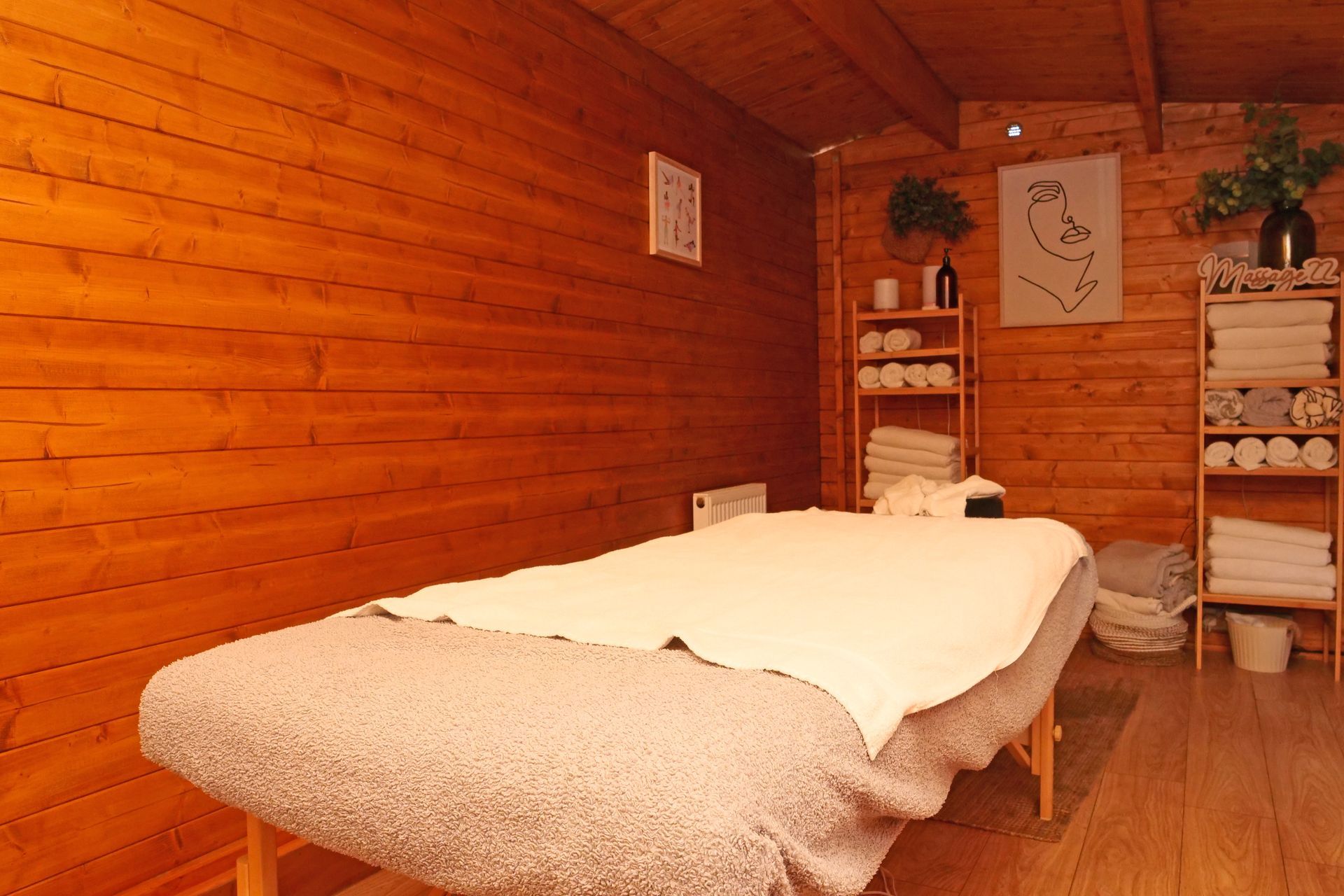 Massage table in a wooden-walled spa room with shelves holding towels and decor.