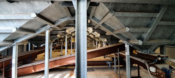 Interno di uno stadio con travi e pilastri in cemento e una zona di posti a sedere o passaggio pedonale parzialmente visibile in costruzione.
