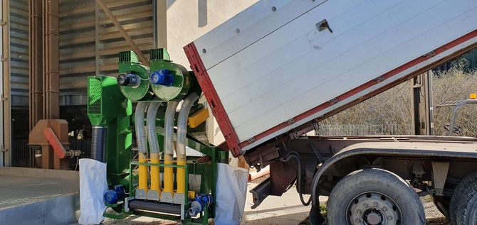 Macchinari industriali verdi accanto a un rimorchio bianco inclinato in un magazzino o in un cortile