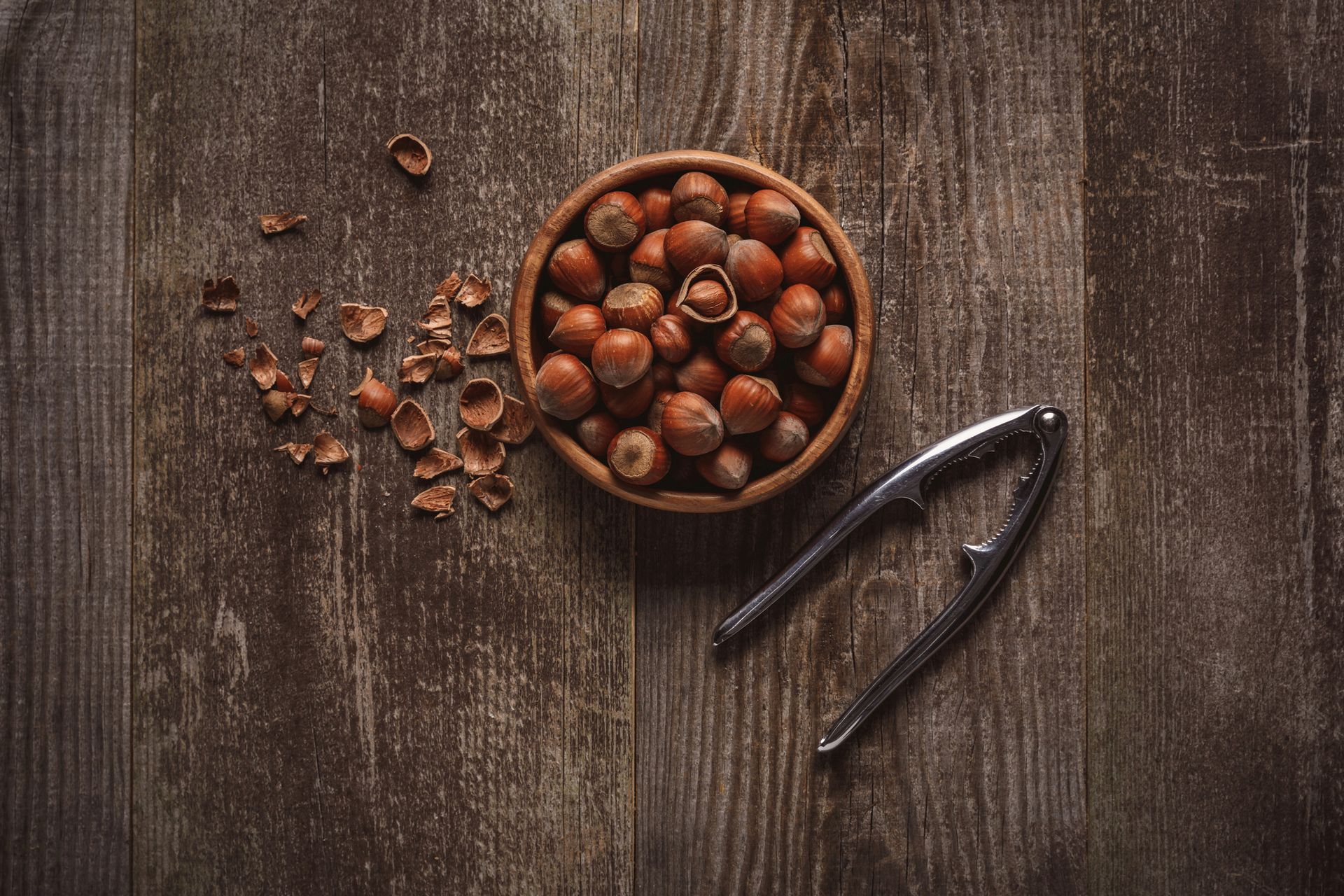 Una ciotola di legno piena di nocciole è posizionata accanto a uno schiaccianoci in metallo su una s