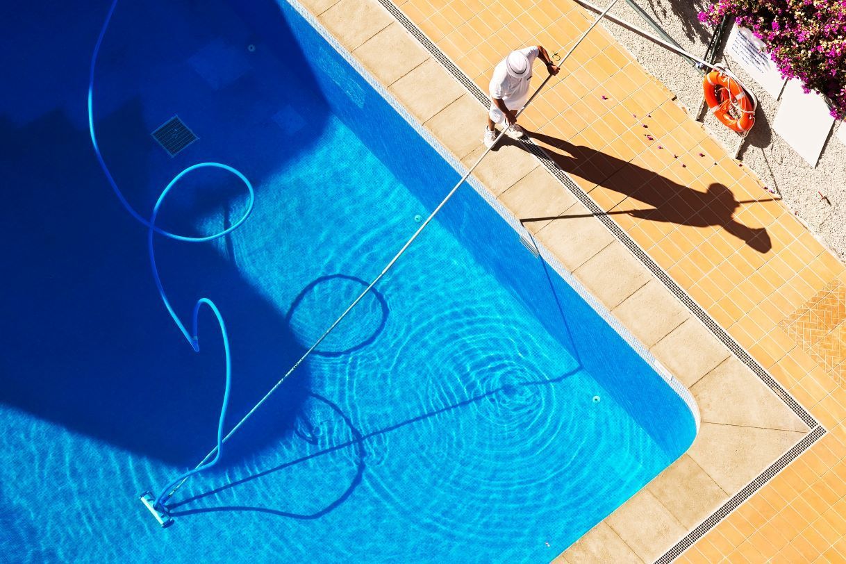 A Man Is Cleaning A Swimming Pool With A Vacuum Cleaner