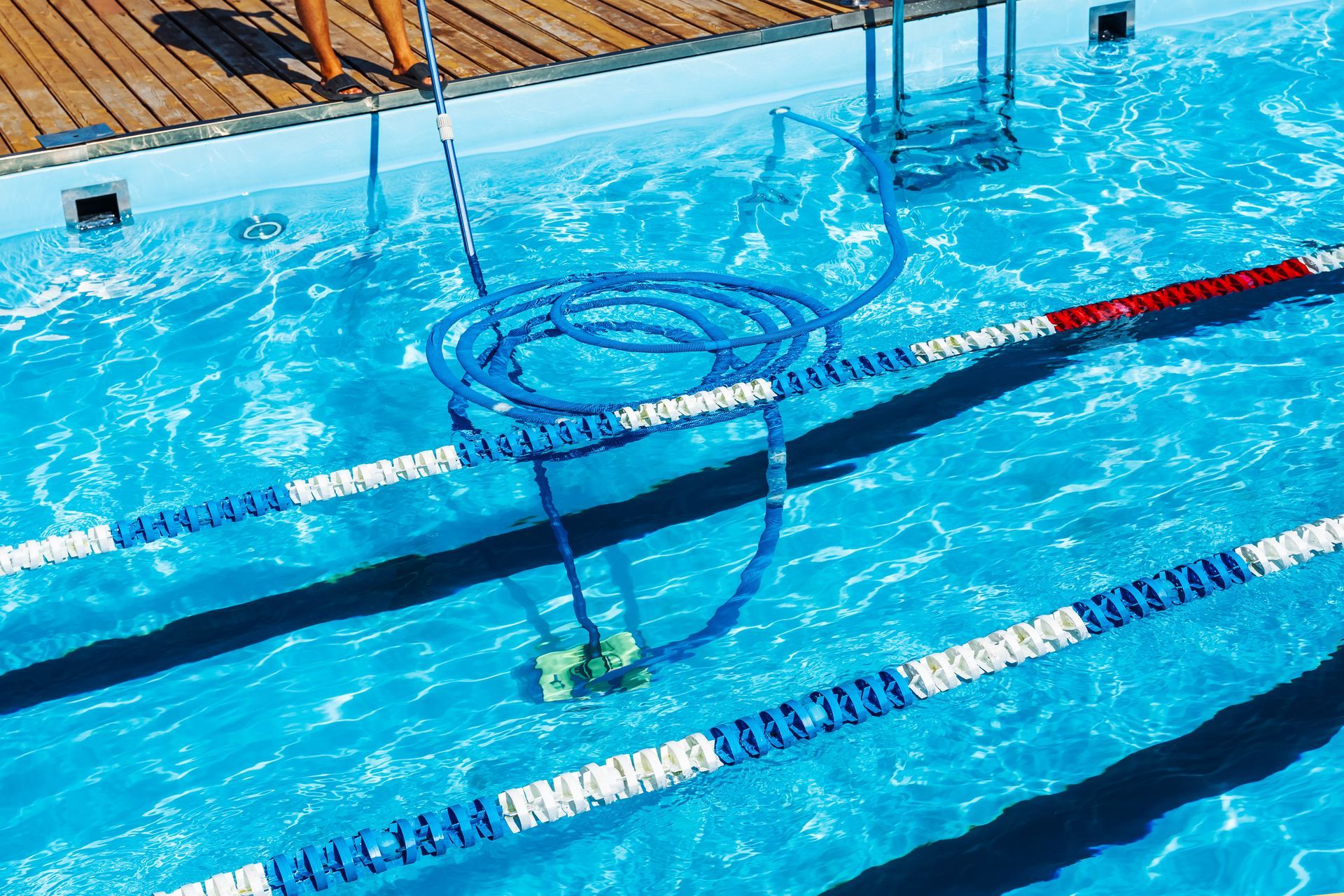 A person is standing next to a swimming pool with a hose attached to it.