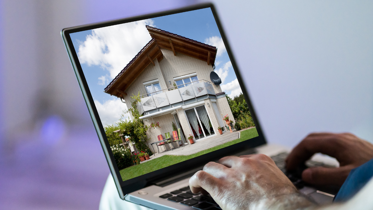Person using laptop, viewing a photo of a two-story house for sale online.