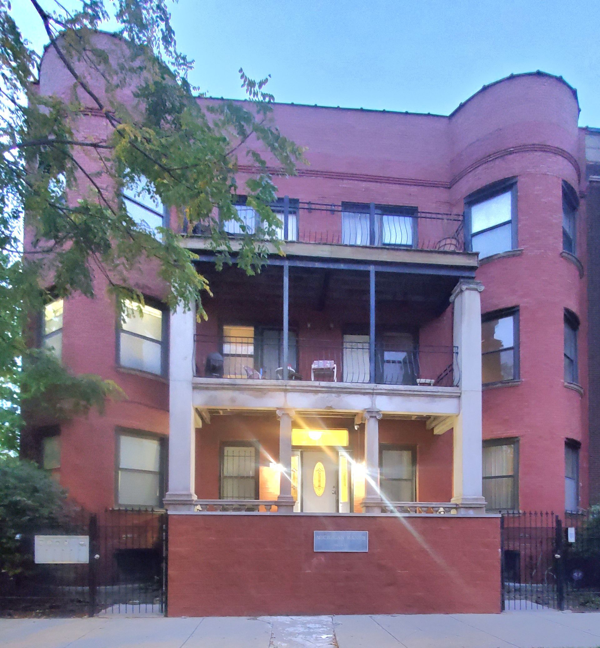 A three-story red brick apartment building with two rounded bays and a central front porch with columns.