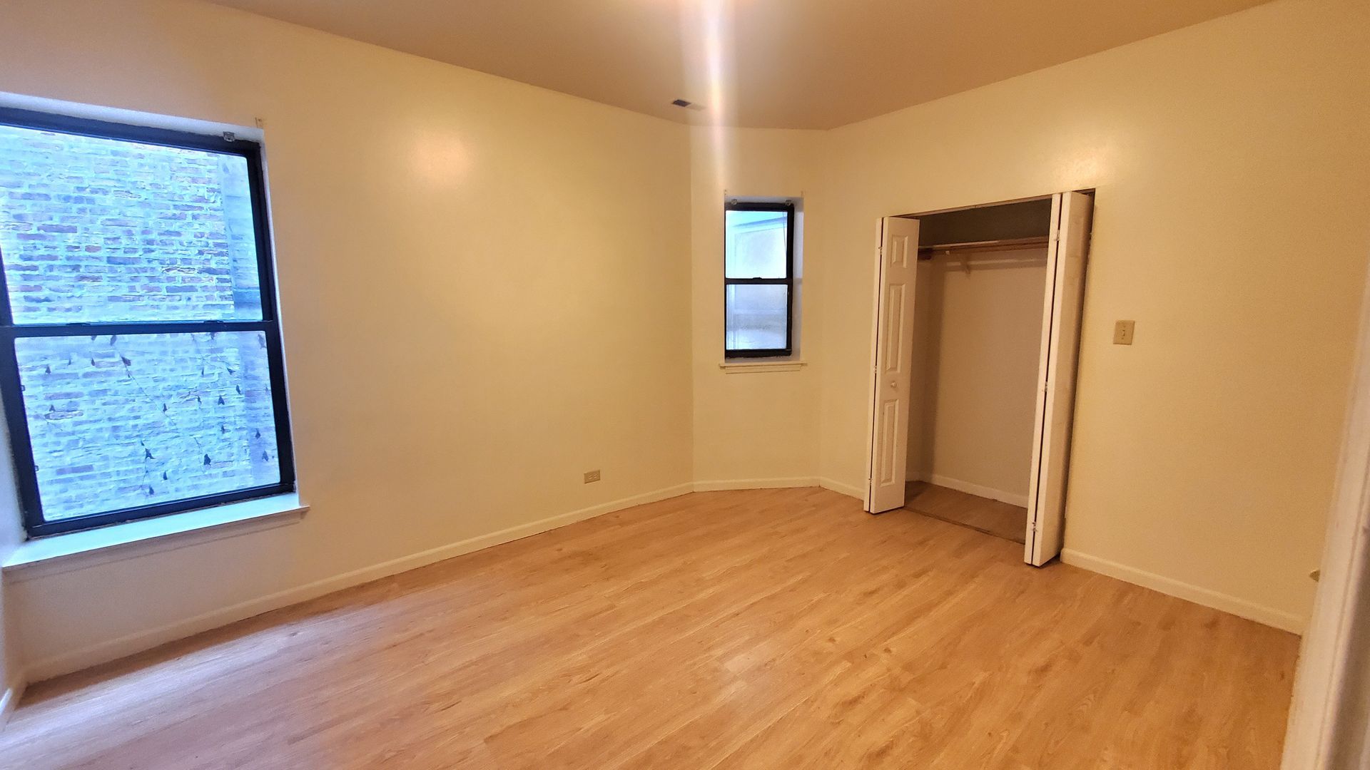 An empty room with light-colored walls, light wood-style flooring, a large window, a small side window, and a closet.