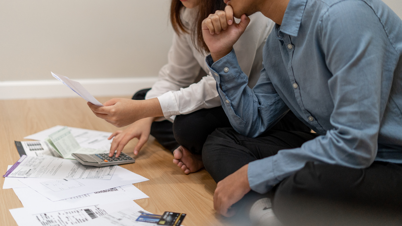 Two people sitting on the floor surrounded by financial documents and a calculator, reviewing papers together.