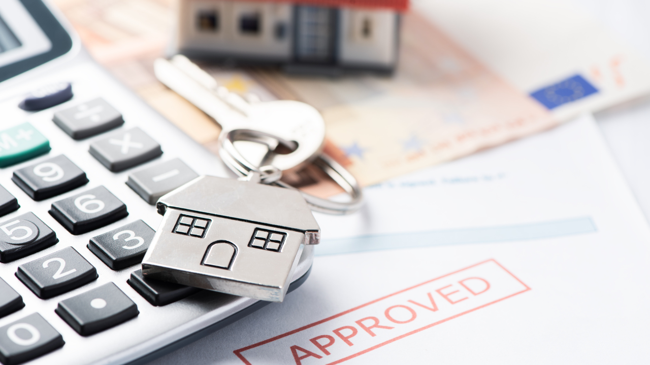 A house-shaped keychain on a calculator, with a toy house and an approved document in the background.