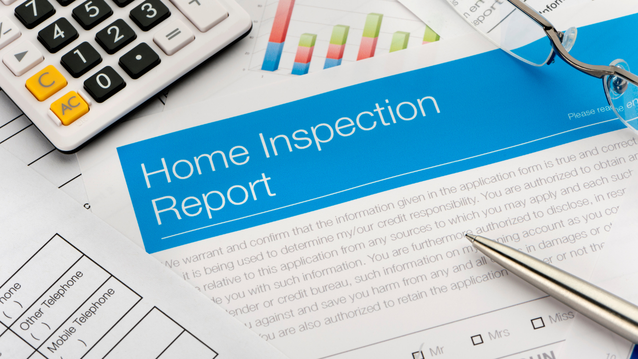 A home inspection report document sits on a desk with a calculator, pen, and eyeglasses, suggesting a financial review.